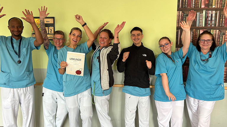 Eine Gruppe von Pflegekräften in blauer Funktionskleidung hält die Arme nach oben und blickt lachend in die Kamera am Internationalen Tag der Pflegenden im Immanuel Haus am Kalksee in Rüdersdorf bei Berlin. Eine Gruppe von Pflegekräften in blauer Funktionskleidung hält die Arme nach oben und blickt lachend in die Kamera am Internationalen Tag der Pflegenden im Immanuel Haus am Kalksee in Rüdersdorf bei Berlin.